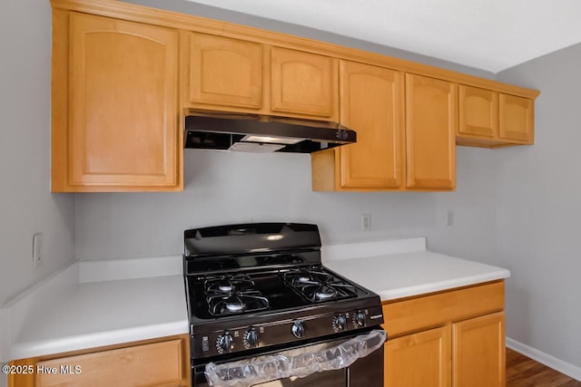 kitchen featuring baseboards, black range with gas stovetop, light countertops, under cabinet range hood, and light brown cabinets