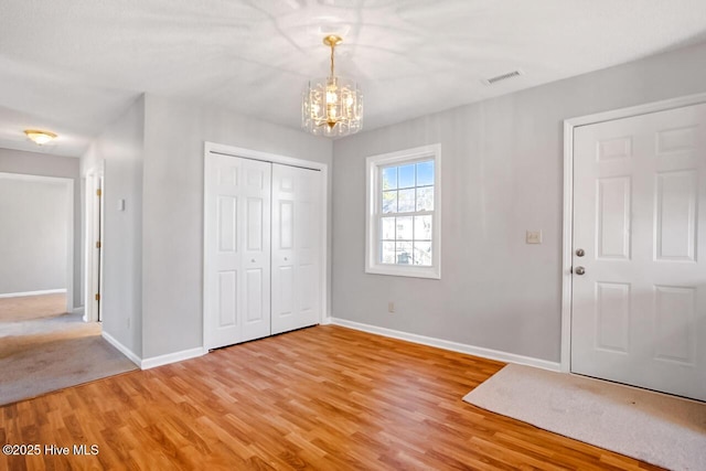 entrance foyer featuring light wood-style flooring, visible vents, a chandelier, and baseboards