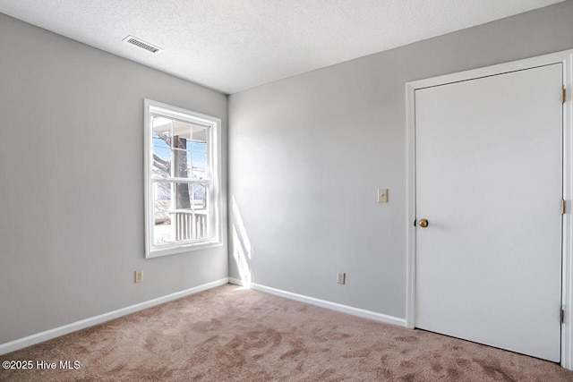 carpeted spare room with visible vents, a textured ceiling, and baseboards