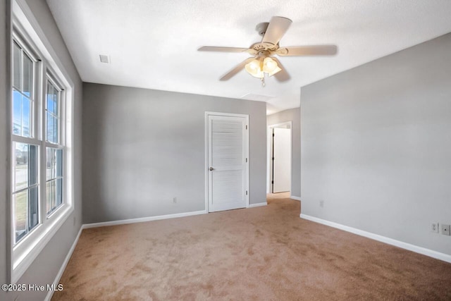 empty room with light colored carpet, ceiling fan, visible vents, and baseboards