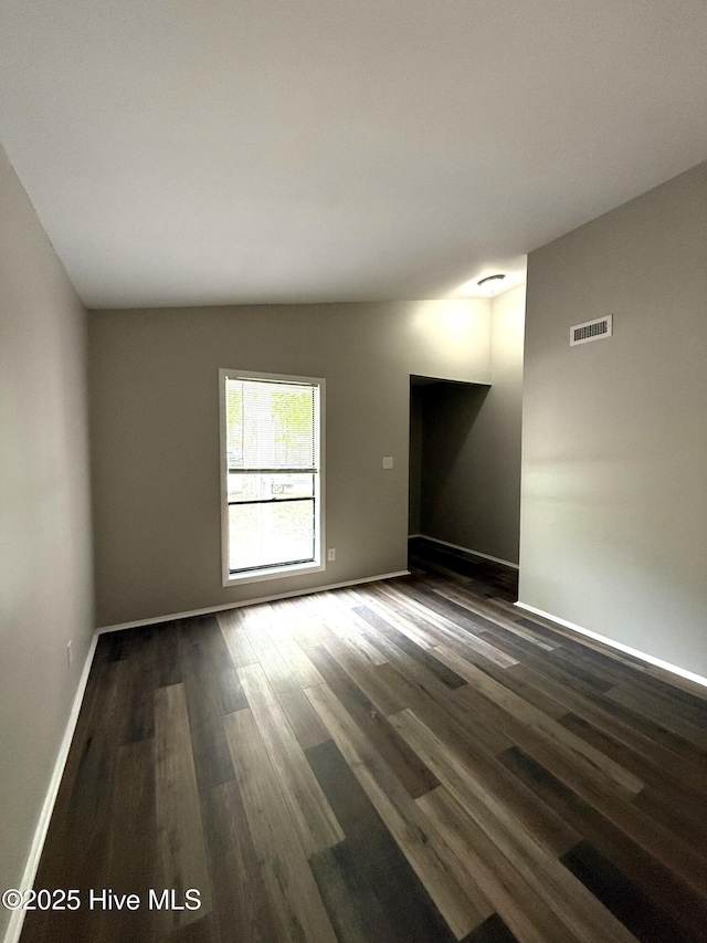 spare room featuring baseboards, visible vents, dark wood-style flooring, and lofted ceiling