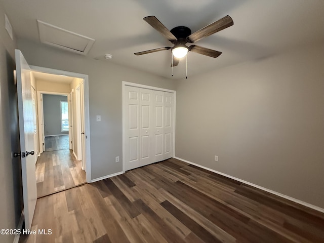 unfurnished bedroom with a closet, attic access, ceiling fan, baseboards, and dark wood-type flooring