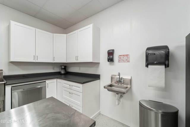 kitchen with a drop ceiling, stainless steel dishwasher, white cabinetry, light speckled floor, and a sink