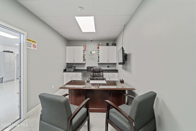 office featuring light speckled floor, built in desk, a paneled ceiling, and baseboards