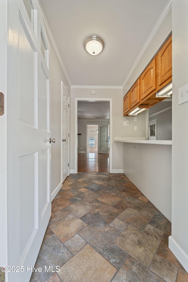 corridor featuring baseboards, stone tile floors, and crown molding