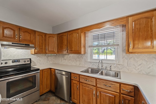 kitchen featuring brown cabinetry, stainless steel appliances, light countertops, under cabinet range hood, and a sink