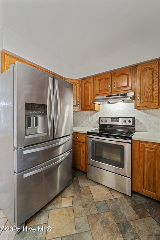 kitchen featuring stone tile floors, stainless steel appliances, decorative backsplash, brown cabinetry, and under cabinet range hood