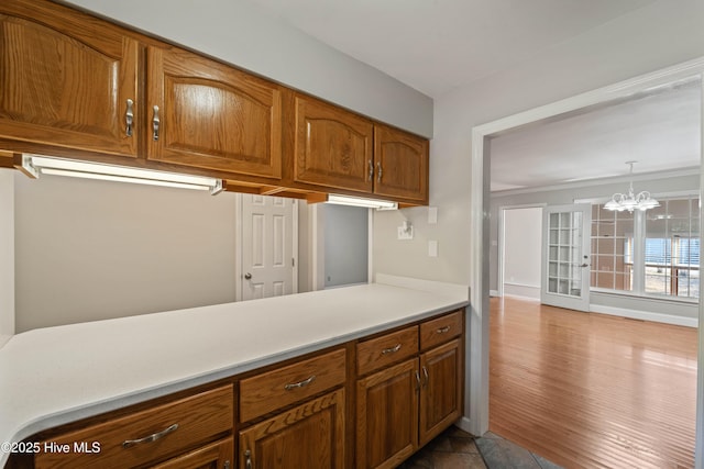 kitchen featuring wood finished floors, baseboards, light countertops, brown cabinetry, and an inviting chandelier