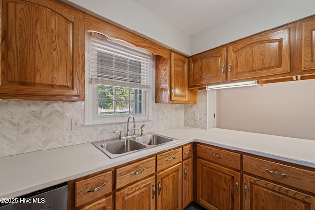 kitchen with brown cabinetry, backsplash, light countertops, and a sink