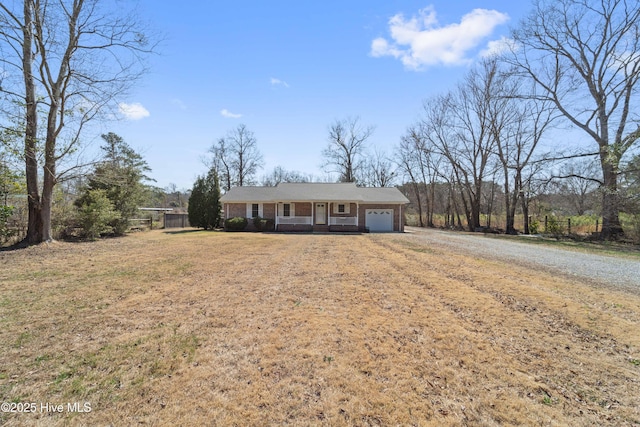 ranch-style home with brick siding, dirt driveway, an attached garage, a porch, and a front yard