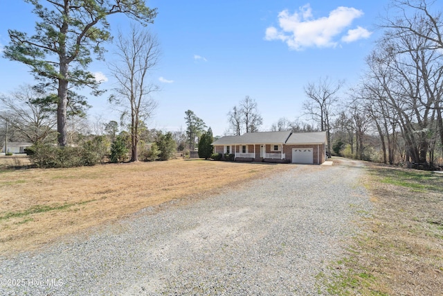 ranch-style home with a garage, brick siding, and gravel driveway