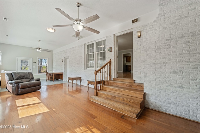 living area with stairs, visible vents, brick wall, and wood finished floors