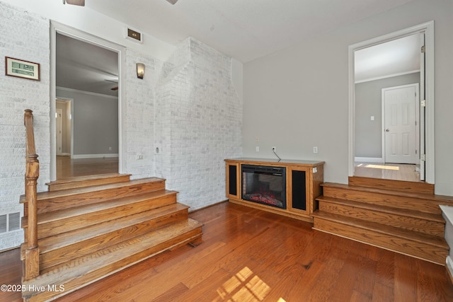 unfurnished living room with a glass covered fireplace, crown molding, stairway, and wood finished floors