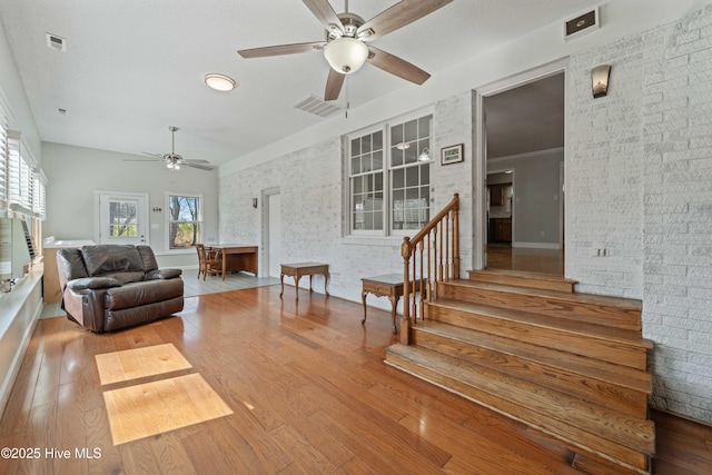 living room featuring wood-type flooring, brick wall, and stairs