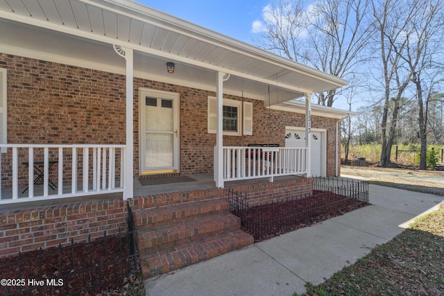 property entrance featuring covered porch, driveway, and brick siding