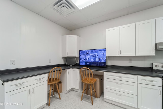 kitchen with a drop ceiling, white cabinetry, built in study area, dark countertops, and stainless steel range with electric stovetop