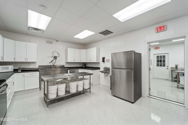 kitchen with visible vents, white microwave, freestanding refrigerator, and white cabinets