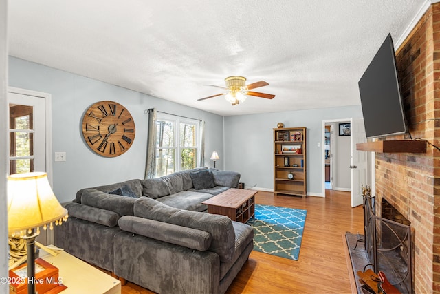 living area with a fireplace, a ceiling fan, a textured ceiling, wood finished floors, and baseboards