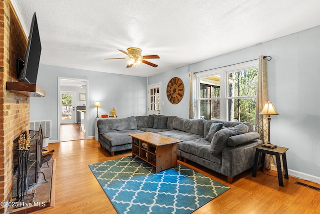 living room with a textured ceiling, light wood-style flooring, a fireplace, visible vents, and baseboards