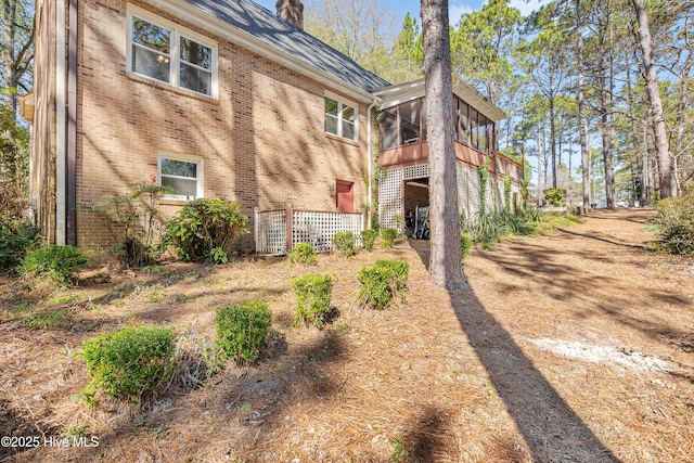 rear view of property featuring a sunroom, a chimney, and brick siding