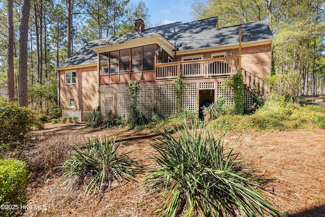 exterior space with brick siding, a chimney, a sunroom, a wooden deck, and stairs