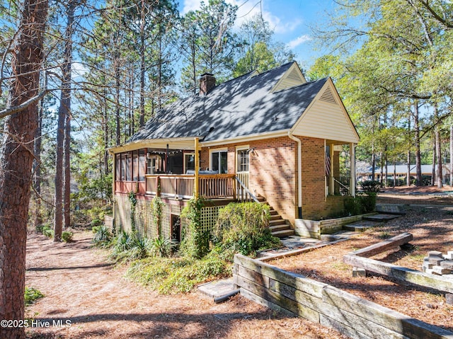 view of front of home with a sunroom, a chimney, stairway, a wooden deck, and brick siding