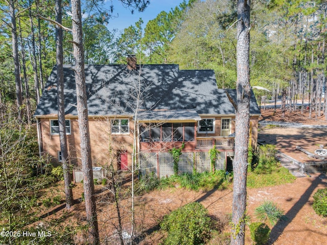 exterior space with brick siding, a chimney, a shingled roof, and a sunroom