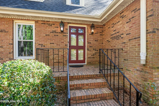 view of exterior entry with brick siding and roof with shingles