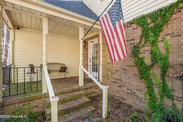 property entrance with covered porch, a shingled roof, and brick siding