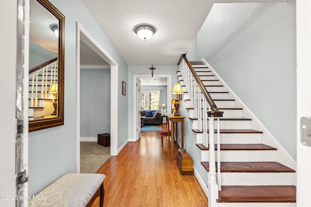 entrance foyer with stairway, a textured ceiling, baseboards, and wood finished floors