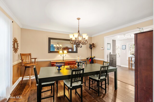 dining room with an inviting chandelier, crown molding, dark wood-style flooring, and a wainscoted wall