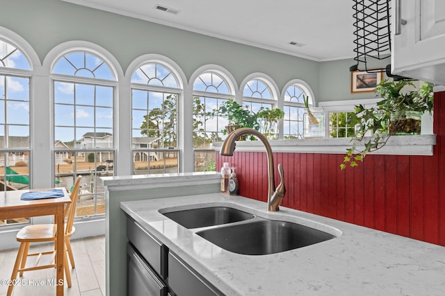 kitchen with crown molding, visible vents, light stone counters, and a sink