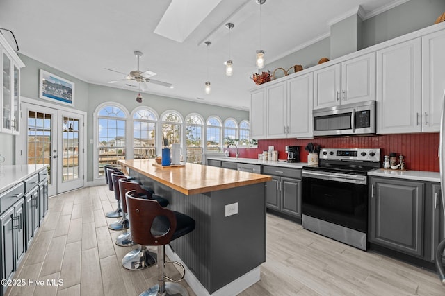 kitchen with a skylight, butcher block countertops, appliances with stainless steel finishes, gray cabinets, and french doors