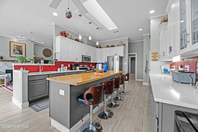 kitchen featuring ceiling fan, gray cabinetry, stainless steel appliances, butcher block counters, and a skylight