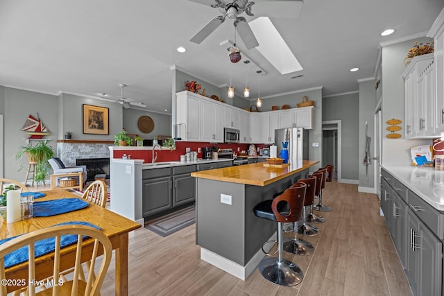 kitchen featuring a skylight, appliances with stainless steel finishes, gray cabinetry, a fireplace, and a sink