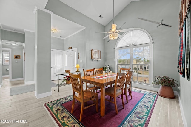 dining room with light wood-style floors, crown molding, baseboards, and high vaulted ceiling