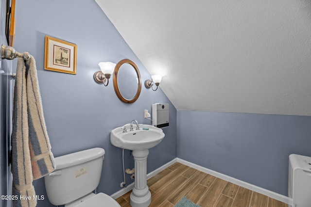 bathroom featuring lofted ceiling, a textured ceiling, toilet, wood finish floors, and baseboards