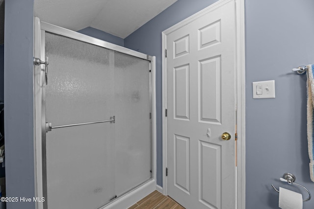 bathroom with a shower stall, vaulted ceiling, and wood finished floors