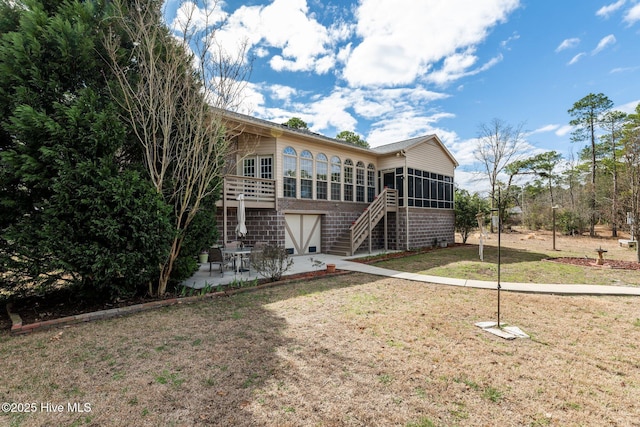 rear view of property featuring a sunroom, a patio area, a yard, and stairs