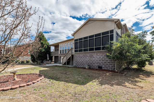 rear view of property with a sunroom, a patio area, a lawn, and stairs