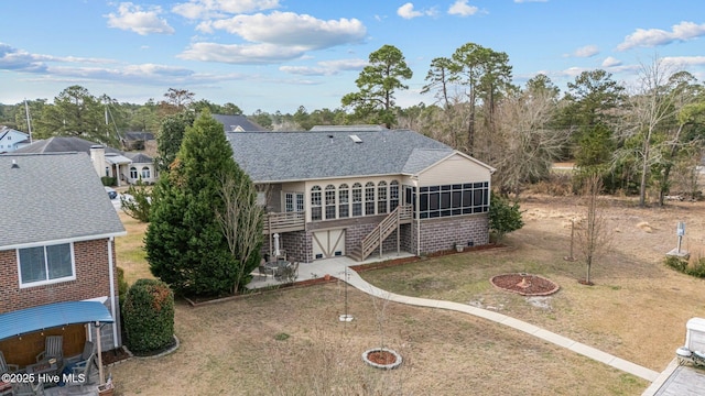 rear view of property with an outdoor fire pit, a lawn, a sunroom, roof with shingles, and stairs