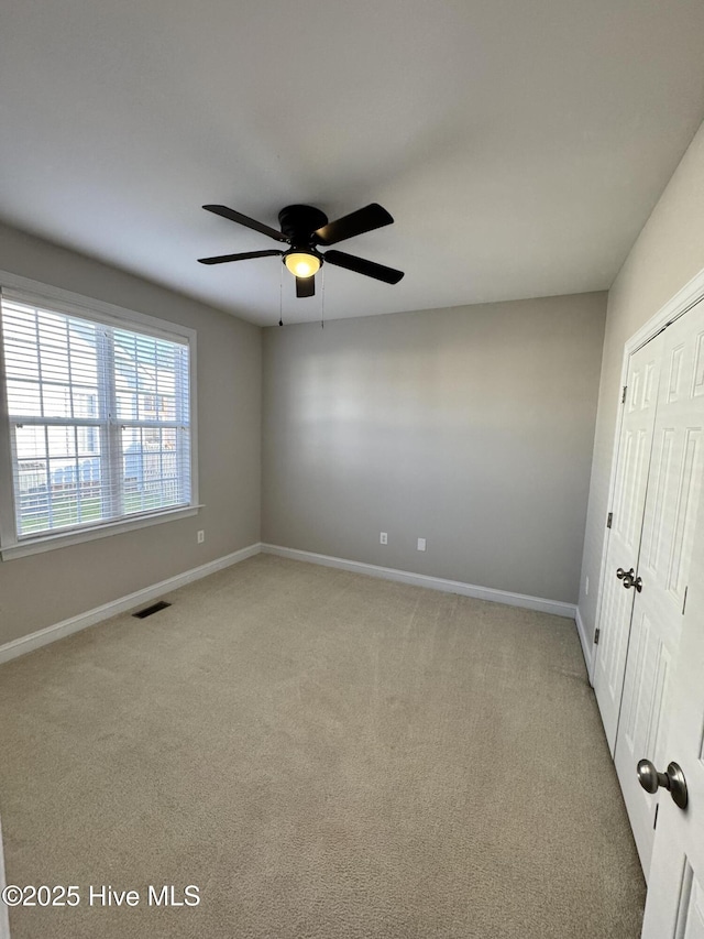 unfurnished bedroom featuring light carpet, baseboards, visible vents, ceiling fan, and a closet