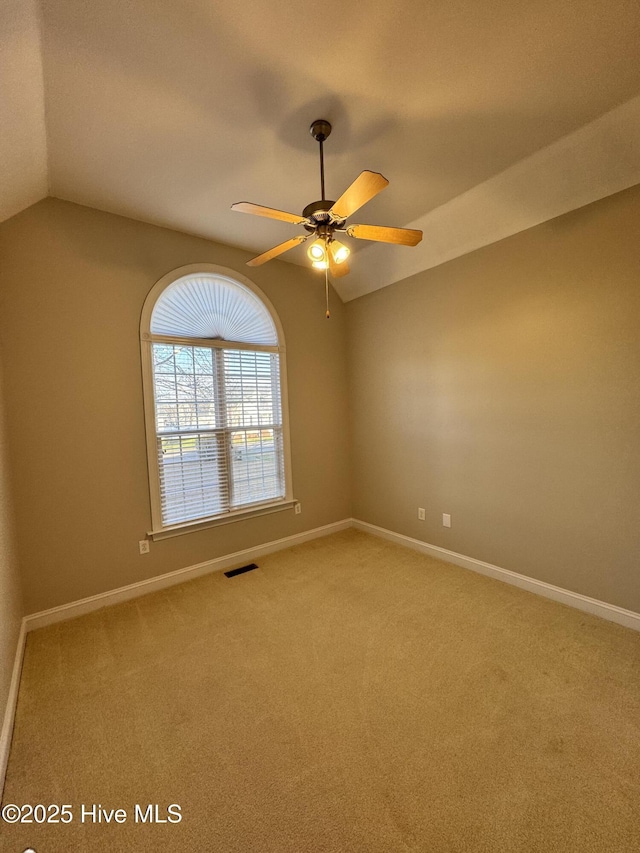 carpeted spare room featuring visible vents, vaulted ceiling, baseboards, and ceiling fan