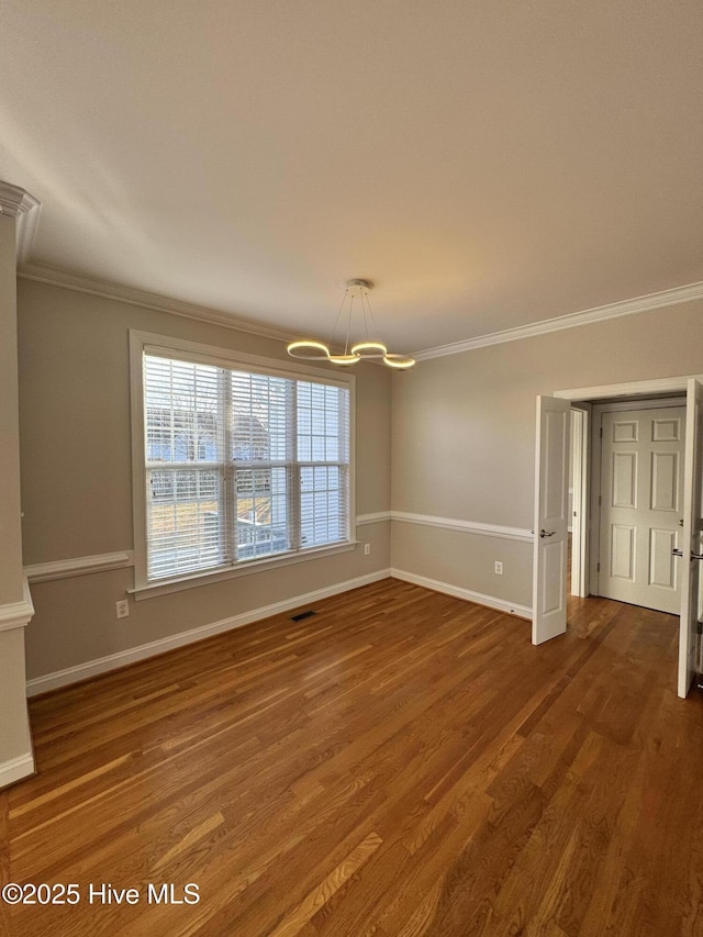 spare room with baseboards, visible vents, wood finished floors, crown molding, and a notable chandelier