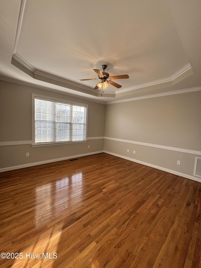 empty room featuring a tray ceiling, wood finished floors, a ceiling fan, and baseboards