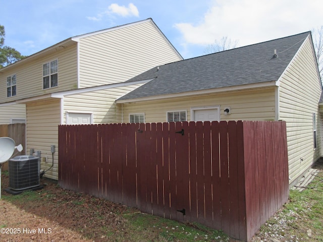 view of property exterior featuring cooling unit, roof with shingles, and fence