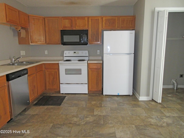 kitchen with light countertops, stone finish flooring, a sink, white appliances, and baseboards