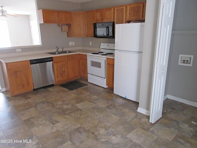 kitchen featuring white appliances, a sink, baseboards, light countertops, and stone finish floor