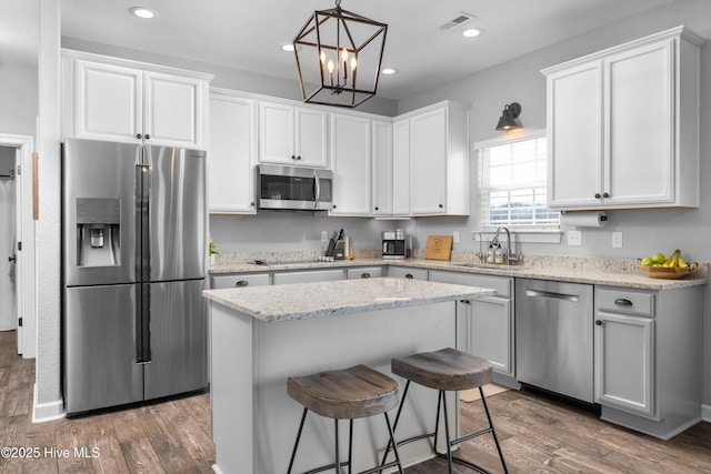 kitchen with visible vents, appliances with stainless steel finishes, wood finished floors, white cabinetry, and a sink