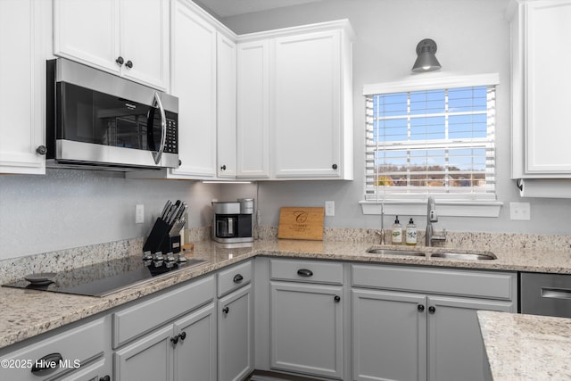 kitchen featuring stainless steel microwave, white cabinets, black electric cooktop, and a sink